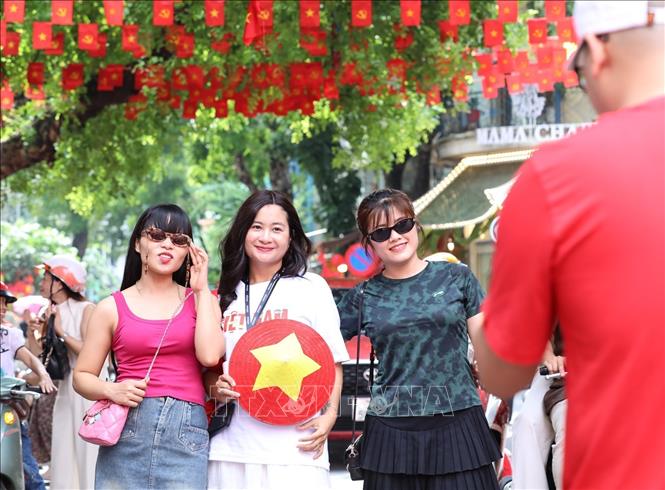 Nhiều người dân lưu lại khoảnh khắc với hình ảnh cờ Tổ quốc tại phố Hàng Mã, phường Hoàn Kiếm. Ảnh: Khánh Hoà - TTXVN