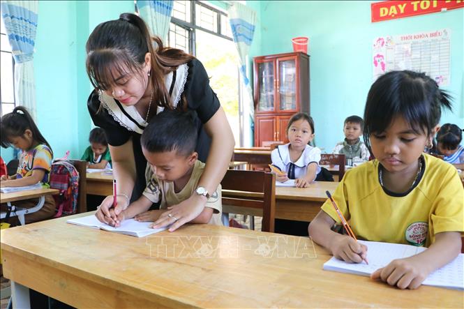 Giáo viên cầm tay hướng dẫn học sinh viết từng nét chữ. Ảnh: Đinh Hương - TTXVN