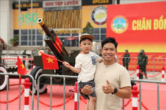Một em bé hào hứng cầm lá cờ Tổ quốc trong vòng tay cha để lưu lại những hình ảnh cùng dàn pháo lễ tại Sân vận động Mỹ Đình. Ảnh: Vũ Quang - TTXVN