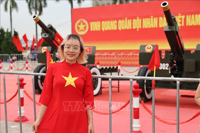 Một bạn trẻ mặc áo dài truyền thống với họa tiết lá cờ Tổ quốc, tươi cười rạng rỡ bên cạnh dàn pháo. Ảnh: Vũ Quang - TTXVN