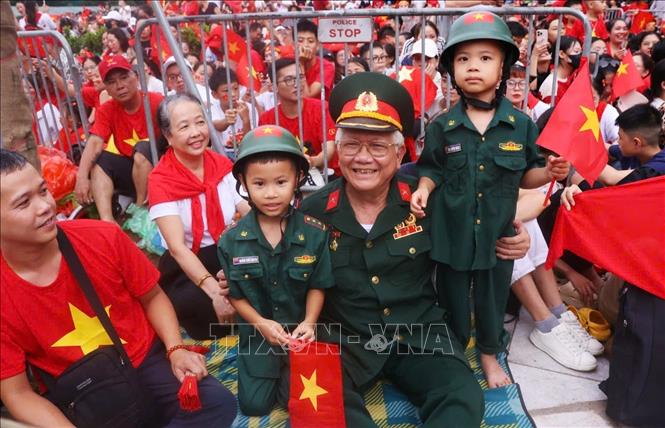 Một cựu chiến binh cùng các cháu đến khu vực ngã tư Hùng Vương - Trần Phú từ sớm để chờ xem màn tổng hợp luyện diễu binh, diễu hành A80 lần thứ 2. Ảnh: Văn Điệp - TTXVN 