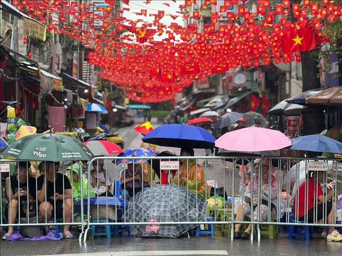 Despite heavy rain, many people line up to secure the best view for A80 parade's preliminary review. VNA Photo
