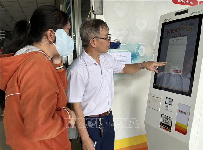 Anh Phan Văn Dũng, chuyên viên công nghệ thông tin - Trung tâm Y tế khu vực Bến Lức hướng dẫn bệnh nhân thao tác trên Ki-ốt nhận diện gương mặt. Ảnh: Đức Hạnh - TTXVN 