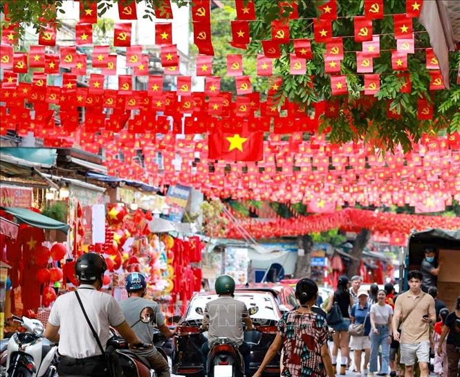Người dân đi dưới bóng cờ hoa ngập tràn sắc đỏ, mang theo tinh thần tự hào Việt Nam khắp các nẻo đường Hà Nội. Ảnh: Thanh Tùng - TTXVN