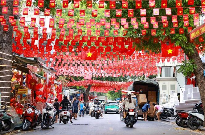 Người dân đi dưới bóng cờ hoa ngập tràn sắc đỏ, mang theo tinh thần tự hào Việt Nam khắp các nẻo đường Hà Nội. Ảnh: Thanh Tùng - TTXVN