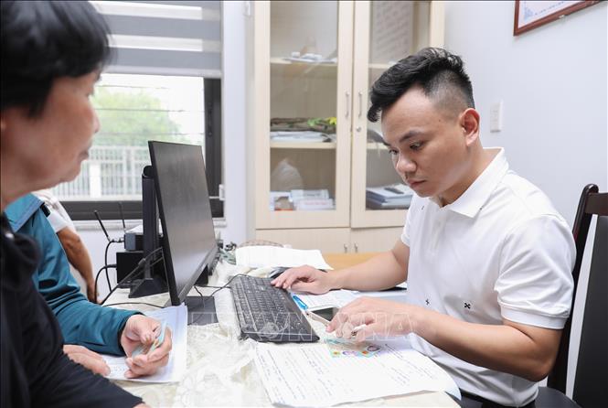 Cán bộ phường Việt Hưng thực hiện thủ tục tra cứu trên máy tính để tiến hành chi trả quà Tết Độc lập cho người dân. Ảnh: Thành Phương - TTXVN