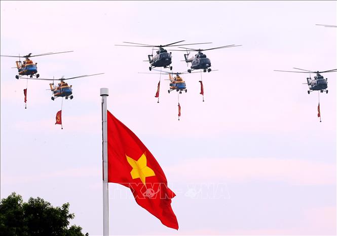 A formation of helicopters of the Air Defense – Air Force carrying the national flag and party flag flies over Ba Dinh Square. 