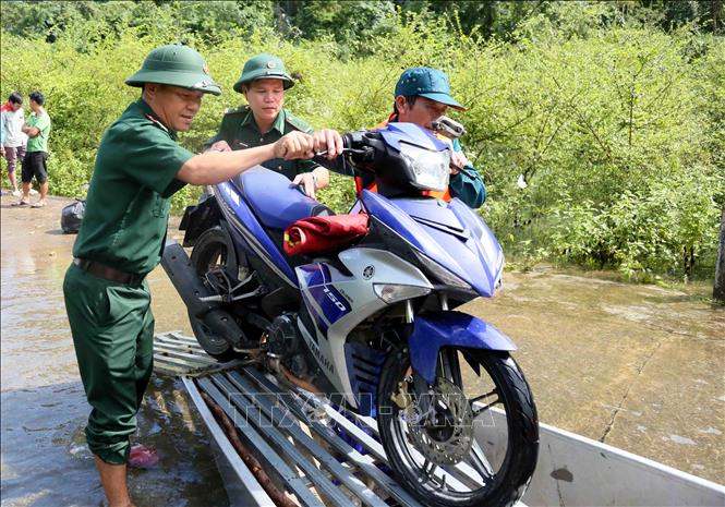 Cán bộ chiến sỹ Đồn Biên phòng Cà Xèng (Ban Chỉ huy Bộ đội Biên phòng Quảng Trị) hỗ trợ người dân đưa xe máy lên thuyền di chuyển qua đoạn ngập. Ảnh: Tá Chuyên – TTXVN
