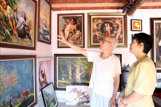 Mr. Pham Van Nghe shows his oil paintings to visitors. VNA Photo: Nguyễn Lành