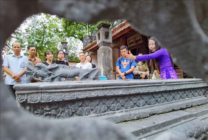 Hướng dẫn viên giới thiệu tới du khách về những nét độc đáo, tinh hoa trong nghệ thuật khắc chạm trên Bảo vật quốc gia “Long sàng”. Ảnh: Thanh Tùng - TTXVN