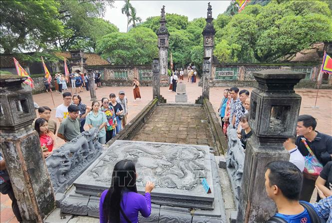 Hướng dẫn viên giới thiệu tới du khách về những nét độc đáo, tinh hoa trong nghệ thuật khắc chạm trên Bảo vật quốc gia “Long sàng”. Ảnh: Thanh Tùng - TTXVN