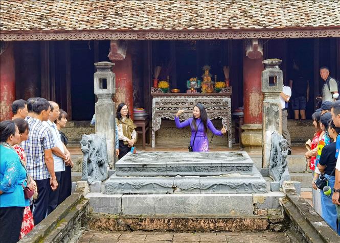 Hướng dẫn viên giới thiệu tới du khách về những nét độc đáo, tinh hoa trong nghệ thuật khắc chạm trên Bảo vật quốc gia “Long sàng”. Ảnh: Thanh Tùng - TTXVN