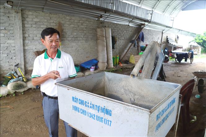 Ông Trần Xuân Sơn bên thiết bị máy cho gà ăn tự động. Ảnh: Xuân Tiến - TTXVN 