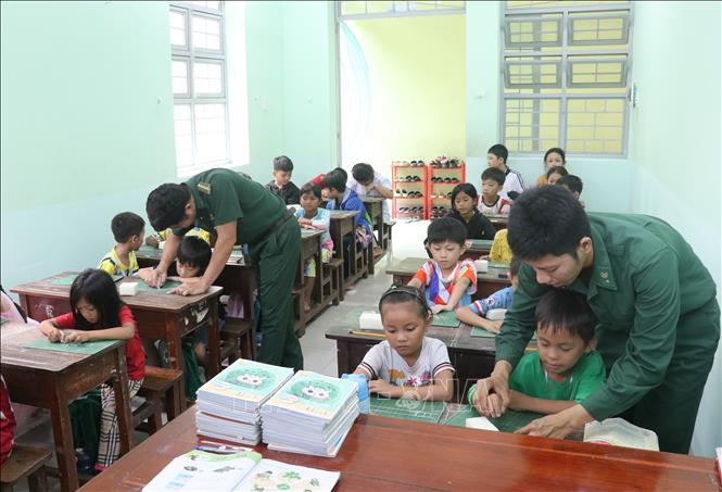 Những người thầy áo xanh tận tình chỉ từng nét chữ cho các em nhỏ. Ảnh: Bùi Giang - TTXVN