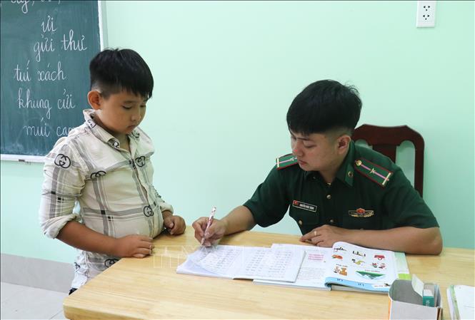 Người lính Biên phòng tận tình chỉ từ nét chữ cho các em học sinh nghèo. Ảnh: Bùi Giang - TTXVN