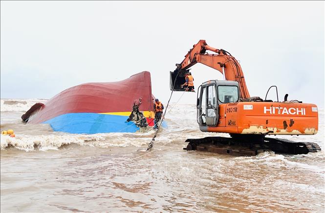Lực lượng cứu hộ sử dụng xe múc để phá vỡ mui tàu, sau đó dùng xe cẩu chuyên dụng kéo toang các mảnh vỏ bằng dây cáp, tạo điều kiện tiếp cận khoang tàu bên trong tàu. Ảnh: Nguyên Linh-TTXVN