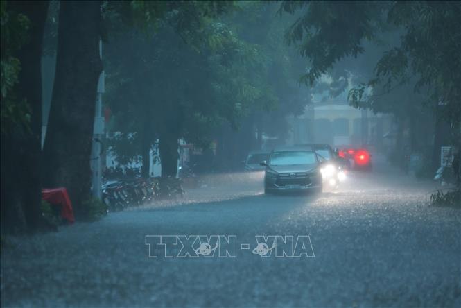Mưa xối xả khiến phố Hàng Bài ngập nặng, ô tô phải bật đèn khi di chuyển. Ảnh: Hoàng Hiếu - TTXVN