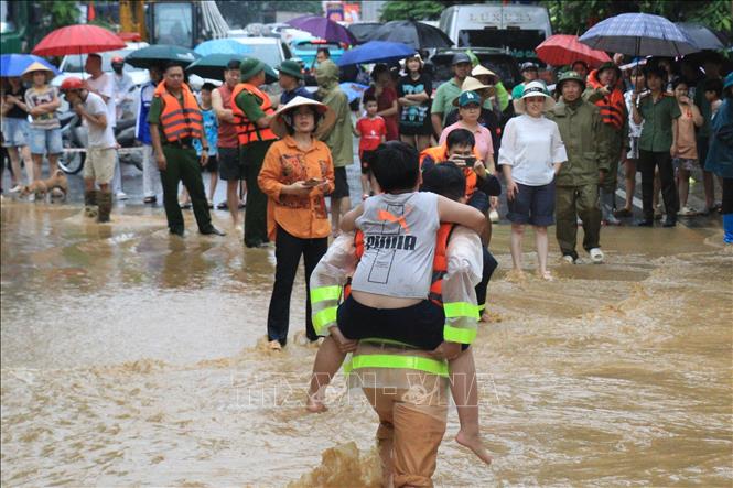 Lực lượng chức năng hỗ trợ em bé di chuyển đến nơi an toàn. Ảnh: Tuấn Anh - TTXVN