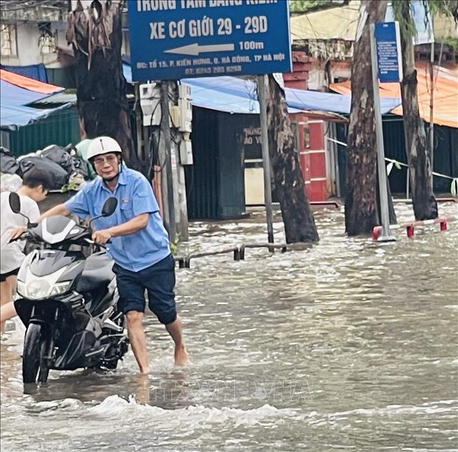 Người dân dắt xe máy bị chết máy khi đi qua điểm ngập trên đường Cầu Bươu. Ảnh: Tuyết Mai - TTXVN


