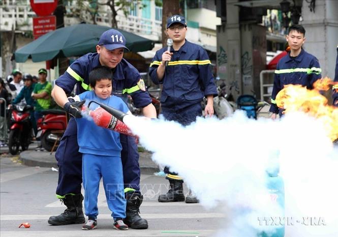 Chiến sĩ cảnh sát PCCC hướng dẫn trẻ em xử lý đám cháy nhỏ ngay tại không gian phố đi bộ hồ Hoàn Kiếm (Hà Nội, 2023). Ảnh: Phạm Kiên - TTXVN