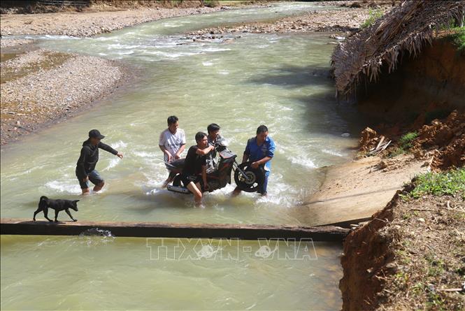  Người dân trong bản hỗ trợ nhau khiêng xe máy qua suối Nậm Ngân. Ảnh: Xuân Tiến - TTXVN 