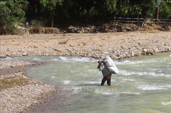  Người dân khó nhọc gùi hàng nặng di chuyển qua suối khi cầu gỗ bắc qua suối đã bị lũ cuốn trôi. Ảnh: Xuân Tiến - TTXVN