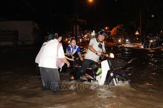 Sinh viên Đại học Cần Thơ giúp người đi xe máy vượt qua đoạn ngập sâu. Ảnh: TTXVN phát