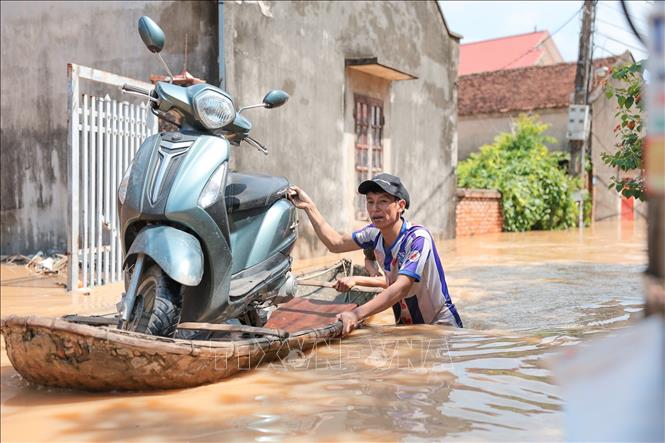 Người dân dùng thuyền di chuyển xe máy qua đoạn ngập sâu tại thôn Ngô Đạo, xã Đa Phúc, Hà Nội. Ảnh: Lê Đông - TTXVN
