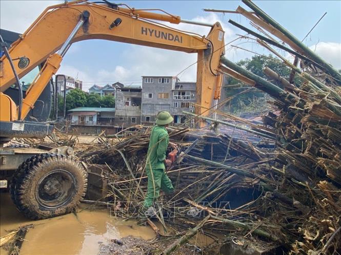 Công nhân phải dùng cưa máy để cắt nhỏ những búi tre mắt kẹt trên Cầu Sông Hiến để máy xúc khơi thông dòng chảy. Ảnh: Quốc Đạt - TTXVN
