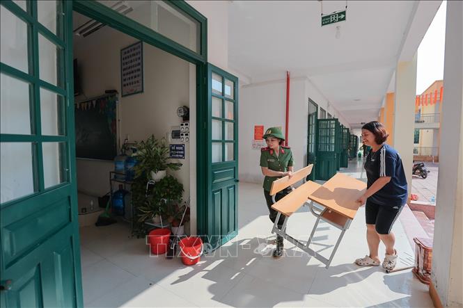 Lực lượng công an hỗ trợ thu dọn, kê lại bàn ghế để sớm đưa trường học vào hoạt động. Ảnh: Lê Đông - TTXVN
