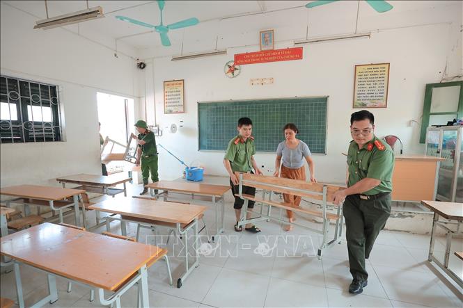 Lực lượng công an hỗ trợ thu dọn, kê lại bàn ghế để sớm đưa trường học vào hoạt động. Ảnh: Lê Đông - TTXVN