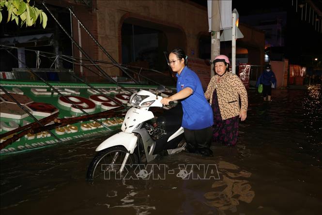 Em Phạm Thảo Trang, sinh viên Trường Đại học Nam Cần Thơ tình nguyện ra hỗ trợ người dân đẩy xe khi triều cường gây ngập sâu trên đường Cách Mạng Tháng Tám. Ảnh: Thanh Liêm - TTXVN