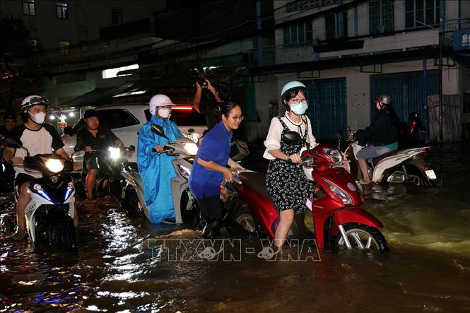 Em Phạm Thảo Trang, sinh viên Trường Đại học Nam Cần Thơ tình nguyện ra hỗ trợ người dân đẩy xe khi triều cường gây ngập sâu trên đường Cách Mạng Tháng Tám. Ảnh: Thanh Liêm - TTXVN