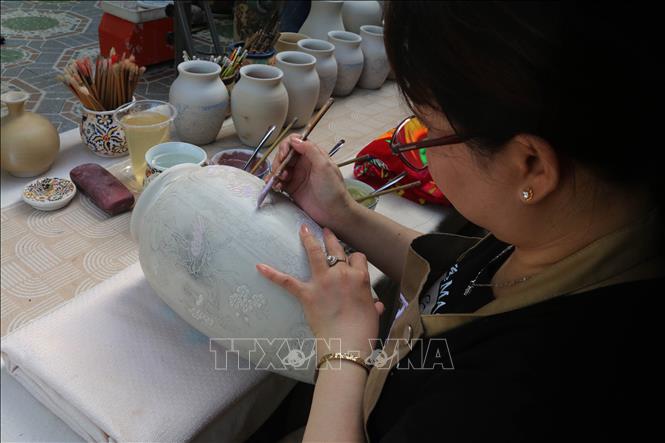 Các nghệ nhân làm gốm ở Đồng Nai thực hiện vẽ màu lên bình gốm. Ảnh: Lê Xuân-TTXVN