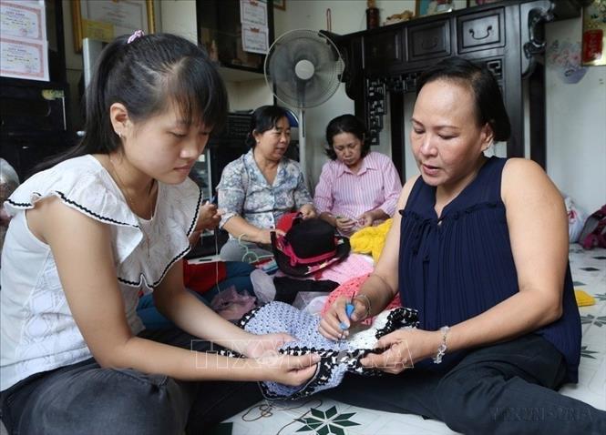 Chị Đinh Thị Tuyết Đào (bên phải) bị bại liệt từ nhỏ, hướng dẫn học viên Cơ sở đan len Phước Đào (174/12 Lê Văn Lương, phường Tân Hưng, quận 7, TP Hồ Chí Minh) học cách móc len. Ảnh: Phương Hoa - TTXVN