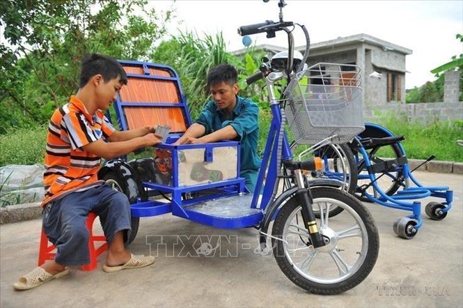 Anh Lê Văn Lịch (bên phải) ở xã Trường Yên, Ninh Bình bị dị tật bẩm sinh, nhưng có ý chí, nghị lực vươn lên, là điển hình làm kinh tế ở địa phương. Từ hộ nghèo, gia đình anh đã có mức sống khá nhờ sản xuất xe lăn điện cho người khuyết tật, được thiết kế riêng phù hợp từng người, đồng thời tạo việc làm cho những người khuyết tật khác. Ảnh: Minh Đức - TTXVN