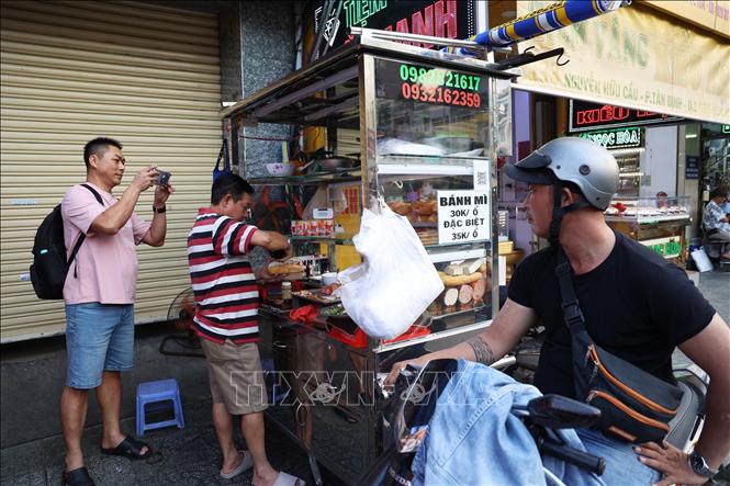 Khách du lịch Trung Quốc ghi lại hình ảnh về món bánh mì mang đặc trưng văn hóa ẩm thực đường phố Việt Nam. Ảnh: Hồng Đạt - TTXVN 
