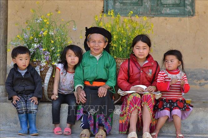 A Mong grandmother and grandchildren in Lung Cam gather in front of the porch of their rammed earth house. VNA Photo: Minh Tâm