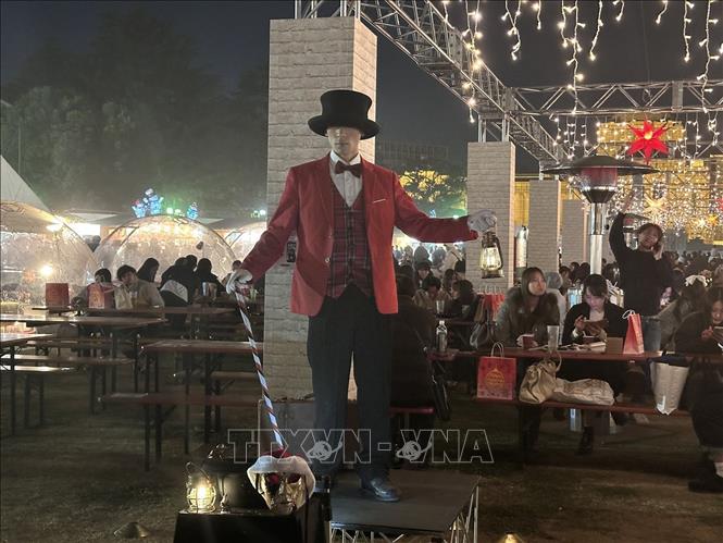 Nghệ sĩ biểu diễn mặc áo đuôi tôm màu đỏ, đội mũ chóp cao màu đen và cầm một cây gậy kẹo tại Chợ Giáng Sinh Tokyo. Ảnh: Nguyễn Tuyến – PV TTXVN tại Nhật Bản