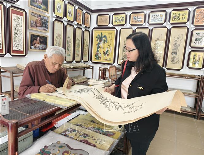 Artisan Nguyen Dang Che signs an autograph for visitors who buys Dong Ho folk paintings. VNA Photo: Thanh Thuong
