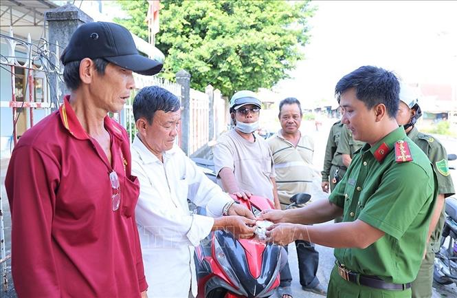 Công an xã Hội An trao những chiếc móc khoá an ninh, có in sẵn số điện thoại trực ban Công an xã cho những người chạy xe dịch vụ khu vực bến phà An Hoà, xã Hội An, tỉnh An Giang. Ảnh: Công Mạo-TTXVN