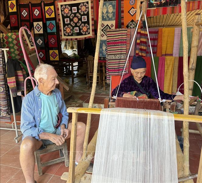 Mr. Roistacher Bob (82 years old), an American tourist, is very impressed with the skillful hands of Mrs. Ha Thi Nhan as she weaves fabric. VNA Photo: Hoa Mai