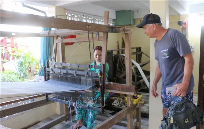 Du khách quốc tế thích thú khi được xem và trải nghiệm quá trình làm ra một tấm thổ cẩm truyền thống của người Chăm tại cơ sở dệt thổ cẩm Mohamach ở ấp Phũm Soài, xã Châu Phong, tỉnh An Giang. Ảnh: Công Mạo-TTXVN