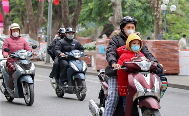 Người dân mặc áo khoác dáng dài và quàng khăn ấm khi di chuyển bằng xe máy qua khu vực hồ Hoàn Kiếm. Ảnh: Vũ Quang - TTXVN