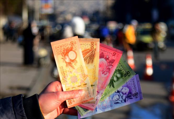 Ngân hàng Trung ương Syria cho biết sau nhiều tháng chuẩn bị, việc đổi tiền Syria cũ lấy tiền giấy mới (ảnh) chính thức bắt đầu vào sáng 3/1/2026. Theo sắc lệnh, tờ tiền cũ sẽ bị loại bỏ đi hai chữ số 0, có nghĩa là cứ 100 bảng Syria cũ sẽ tương đương với 1 bảng Syria mới. Việc phát hành đồng tiền mới được xem là bước đi quan trọng trong quá trình tái lập ổn định tài chính và khôi phục niềm tin vào hệ thống kinh tế của Syria. Ảnh: THX/TTXVN