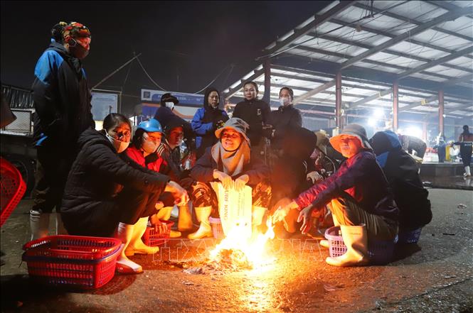 Phụ nữ làng biển và các tiểu thương đi chợ Lạch Vạn đốt lửa sưởi ấm trong thời gian chờ đợi tàu, thuyền cập bến. Ảnh: Xuân Tiến - TTXVN 