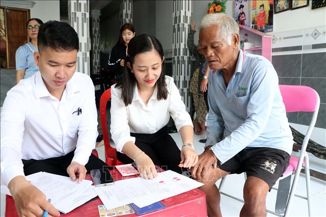 Công chức phường Sóc Trăng hỗ trợ người cao tuổi khó khăn vận động thực hiện các thủ tục ủy quyền nhận trợ cấp. Ảnh: Trung Kiên - TTXVN