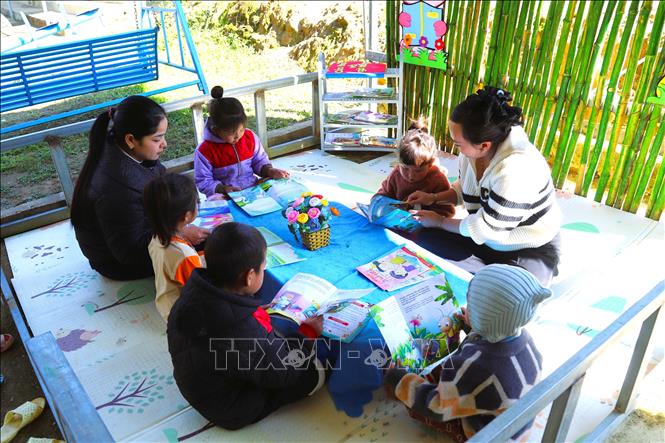Hai cô giáo Nguyễn Thị Trâm, Ngân Thị Chiến, giáo viên cắm bản tại điểm trường Mầm non Huồi Măn hướng dẫn các cháu học trò trong tiết học ngoại khóa, xem tranh ảnh. Ảnh: Xuân Tiến - TTXVN 