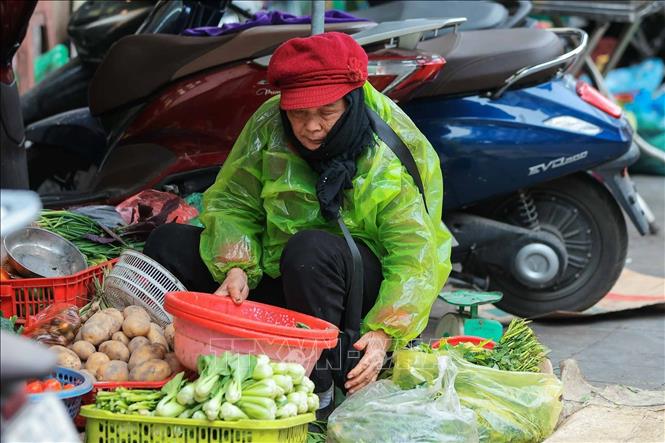 Một nguời bán hàng chợ Đồng Xuân phải mặc thêm áo mưa chống rét. Ảnh: Hoàng Hiếu - TTXVN