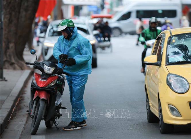 Một lái xe công nghệ phải mặc thêm áo mưa để chống rét khi nhiệt độ Hà Nội giảm rõ rệt. Ảnh: Hoàng Hiếu - TTXVN
